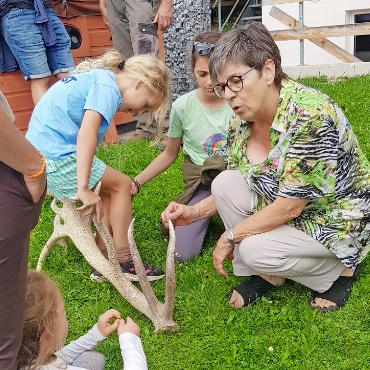 Rothirsch Leon empfängt Feriengäste - Links: Christine Haldi erklärt den Kindern den aus Knochensubstanz jährlich neu gebildeten Kopfschmuck männlicher Hirsche.
