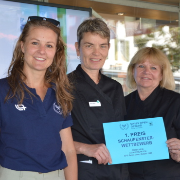 Murmeli-Tennis im Schaufenster gewinnt - Selina Flückiger übergibt im Auftrag des Swiss Open Gstaad den Preis für das am schönsten gestaltete Schaufenster an die beiden strahlenden Siegerinnen Sandra Walker und Susanne Kübli, die eine Murmeltiertennisszene in der Apotheke Dr. Kropf. (Foto: AvS)