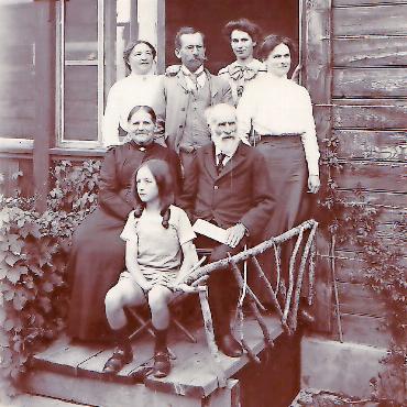 Ölbild von François Furet: Kunstwerk und Zeitdokument - Die Familie von Christian und Catherine Bratschi vor dem Haus am Oberbort, um 1910. In der Mitte Sohn Paul, der als Amateurfotograf tätig war, mit seiner Frau Stéphanie Georgewski, vorne deren Tochter Germaine, rechts die beiden Töchter Julia und Marguerite Bratschi. Die Eingangstreppe ist noch provisorisch. FOTO: ZVG