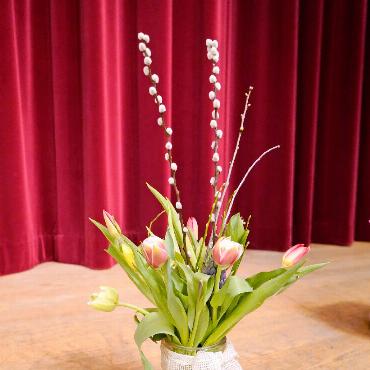 Übergabe des Dirigentenstabs und ein witziger Zweiakter - Eines der unzähligen schönen Blumengestecke, die den Bühnenrand zierten.