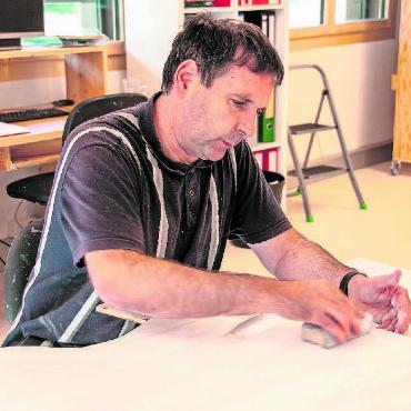 Grosse Begeisterung in den neuen Werkstätten der Alpenruhe - Reinhard R. arbeitet vorwiegend im Mal- und Holzatelier. Hier werden die in der Schreinerei gefertigten Strassenfiguren, Holzpuzzles und die vielseitigen Kundenwünsche geschliffen, bemalt und zur Auslieferung fertiggemacht. Für die beliebten K-Lumet (Anzündhilfen) werden die Hölzli vorbereitet und zusammengestellt. Die fertigen K-Lumet gingen dann noch nach Frutigen, wo sie in Wachs getränkt würden, erzählt er. Er lässt verlauten, dass er jetzt seit zwei Jahren in der Woche dreieinhalb Tage hier arbeite, aber in der Mettlen wohne. Den Rest der Woche könne er glücklicherweise in seinem Beruf als Hochbauzeichner arbeiten. «Während dem Umbau war es in den Containern sehr eng, hier sind jetzt die Räume wieder viel grösser und heller», strahlt Reinhard.