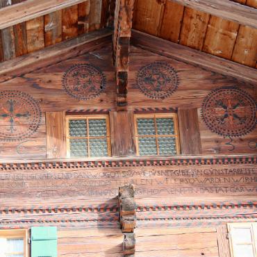 Glodo Dubach und die königlichen Blüten am Säumerweg - Die Rosette ist ein Rundmotiv, das auf den Fassaden alter Bauernhäuser als Verzierung eingesetzt wurde. Oft besteht sie aus acht Lilienblüten, die strahlenförmig von einem zentralen Punkt ausgehen und schwarz und rot ausgefärbt sind. Auch bei neuen Chalets ist sie beliebt.