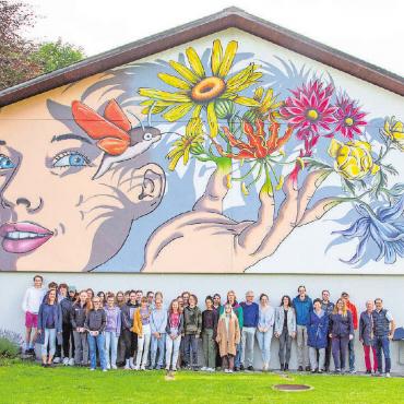 Mit einem bunten Blickfang die Bekanntheit steigern - Die Schülerinnen, Schüler und Lehrpersonen des Gymnasiums Interlaken, Abteilung Gstaad, vor dem neuen Wandgemälde. FOTOS: JOCELYNE PAGE