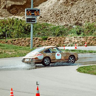 Zehn Jahre: Gstaad Palace Challenge feiert Jubiläum - Ein klassischer Porsche meistert den Handling-Parcours – eine der anspruchsvollen Prüfungen der Rallye. Kleines Foto: Ein junges Mädchen in traditioneller Tracht schwenkt die Zielflagge vor dem offiziellen Zielbogen der Gstaad Palace Challenge.