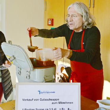 Diskrete Helfer - Pfarrer Bruno Bader schöpft die inzwischen fast schon ein wenig berühmte Gulaschsuppe in die mitgebrachten Gefässe der Besucher.