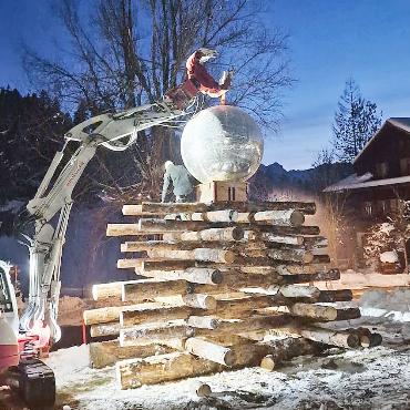 Weihnachtsbaum aus Holz und Discokugel - Mithilfe des Baggers wird die zwei Meter hohe Discokugel auf den Holzweihnachtsbaum gesetzt. Kleines Bild: Der Baum wird zurechtgesägt. FOTOS: ZVG
