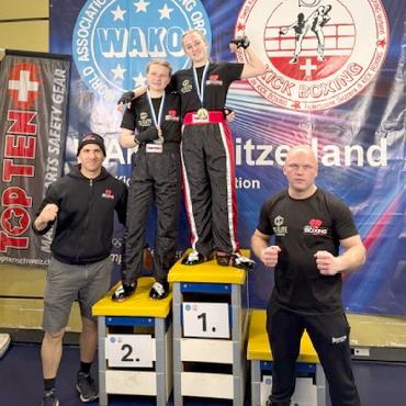 Gstaad Kickboxing glänzt beim 4. Basler Dynamic Cup - Im spannenden Finalkampf standen sich Alina Kohli und Lynn Hefti gegenüber – wenig später vereint auf dem Siegerpodest. Begleitet wurden sie von den Assistenztrainern Themi (mit Hut) und Kamil.