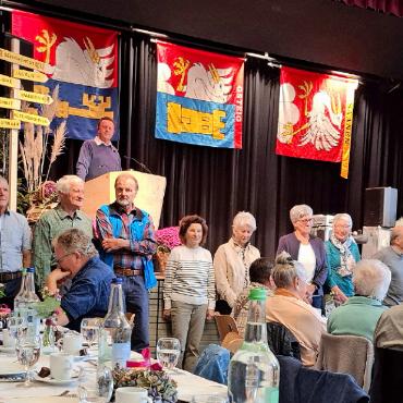 «Altes Eisen ist sinnvoll» - Die Mitglieder des Seniorenrats stehend vor der schön geschmückten Tribüne: v.r. Hansjörg Zahnd, Gemeinde Saanen, Brigitte Perreten und Rosmarie Addor, beide Gemeinde Lauenen, Therese Baumgartner, Susanne Perreten, Peter Zingre, Bruno Haldi, Emil Trachsel, Beatrice Bäriswyl, Sekretärin und Leiterin Soziales, und am Rednerpult Präsident Ueli Müller, alle Gemeinde Saanen. Entschuldigt waren Nadia Oberli und René Chapuis, Gemeinde Gsteig. FOTO: LÉONIE MÜLLER