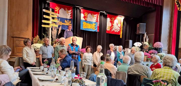 Die Mitglieder des Seniorenrats stehend vor der schön geschmückten Tribüne: v.r. Hansjörg Zahnd, Gemeinde Saanen, Brigitte Perreten und Rosmarie Addor, beide Gemeinde Lauenen, Therese Baumgartner, Susanne Perreten, Peter Zingre, Bruno Haldi, Emil Trachsel, Beatrice Bäriswyl, Sekretärin und Leiterin Soziales, und am Rednerpult Präsident Ueli Müller, alle Gemeinde Saanen. Entschuldigt waren Nadia Oberli und René Chapuis, Gemeinde Gsteig. FOTO: LÉONIE MÜLLER