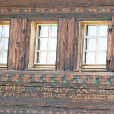 Das «einfache» Haus, zwei ungleiche Wohnstuben und der Losbub - Die Inschrift in Antiqua war nur noch undeutlich erkennbar und wurde daher teilweise nachgeschnitzt. Ein Ausschnitt aus dem längeren Hausspruch: WIER BVWEN ALHIER HÜSER UND PALEST UND SIN DOCH HIE NUR GEST UND DA WIR NIT HIER EWIG SIN DA BVWEN WIR GANZ WENIG HIN