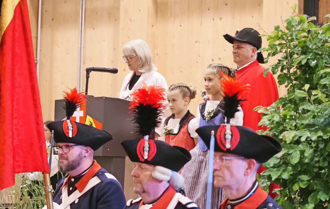 Grossratspräsidentin Anne Speiser mit ihren beiden Grosstöchtern Joëlle (8) und Zoé (11) bei ihrer Ansprache, begleitet vom Staatsweibel und der Ehrenformation. Grossratspräsidentin Anne Speiser mit ihren beiden Grosstöchtern Joëlle (8) und Zoé (11) bei ihrer Ansprache, begleitet vom Staatsweibel und der Ehrenformation.